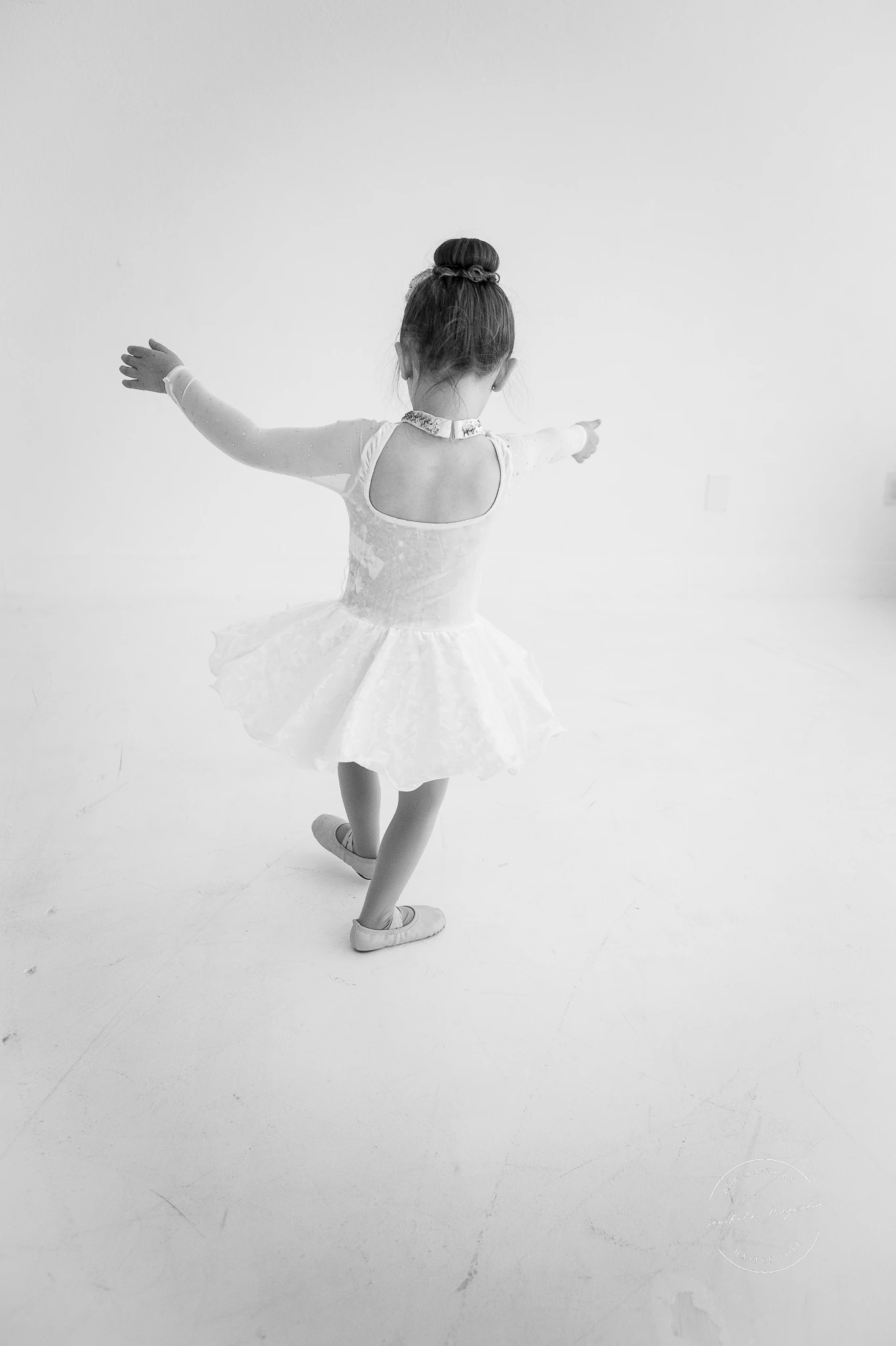 A preschool dancer in a white tutu practicing a ballet pose
