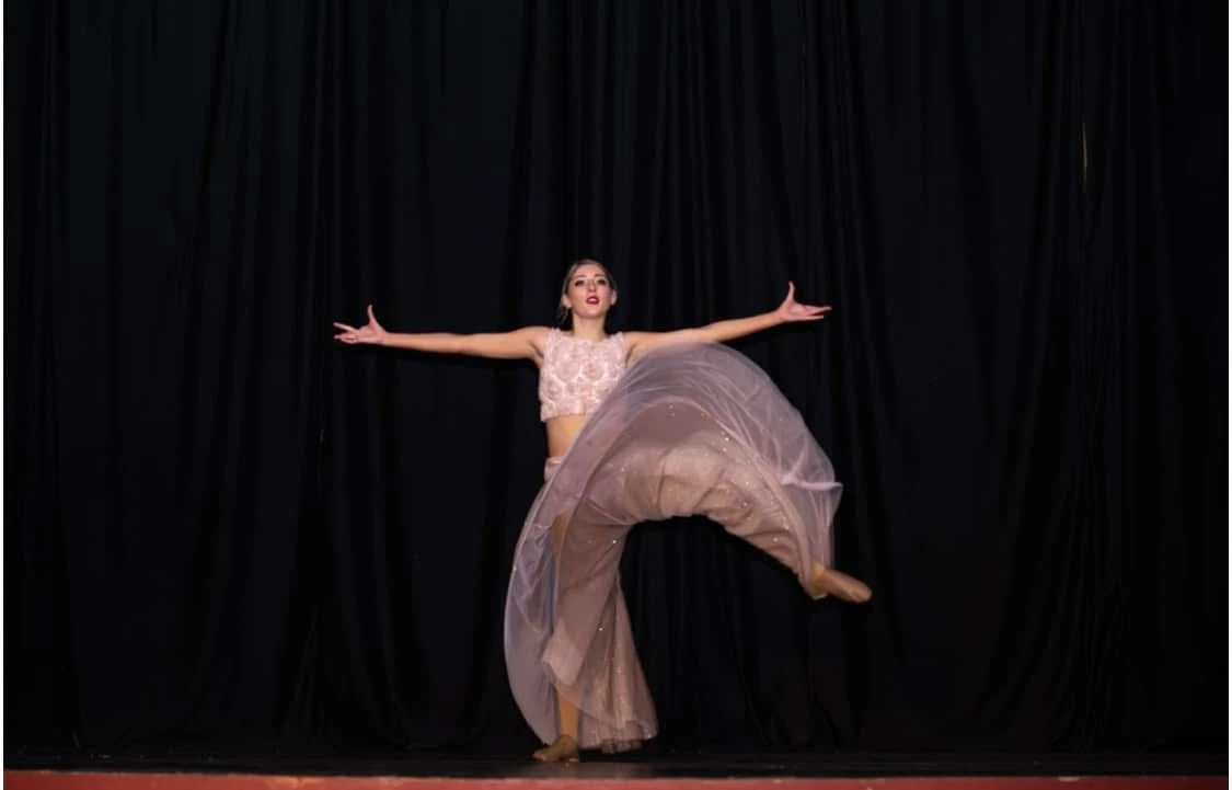 A solo dancer performing a leap on stage in a flowing costume
