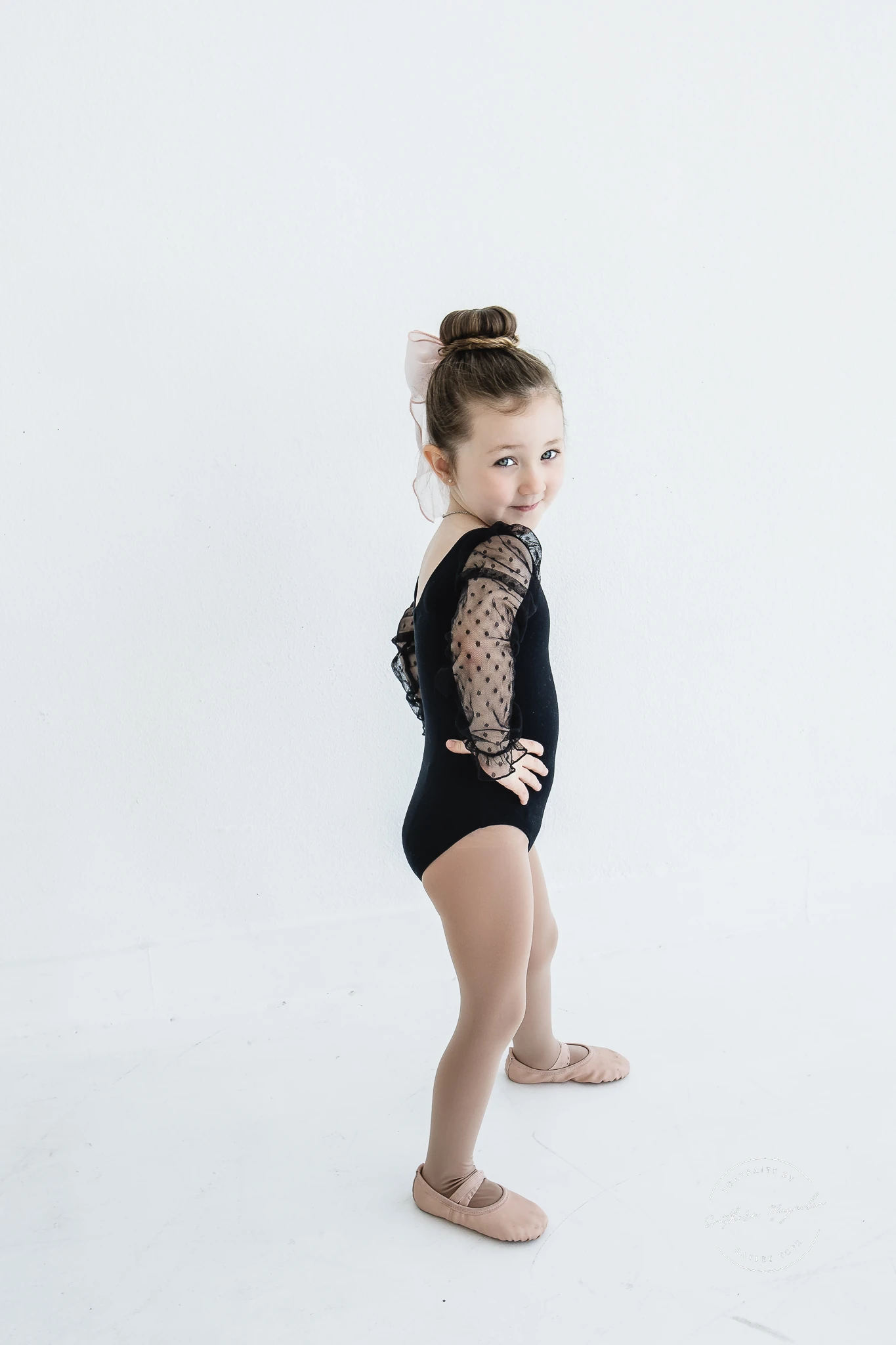 A young dancer in a black leotard posing during a studio photo session