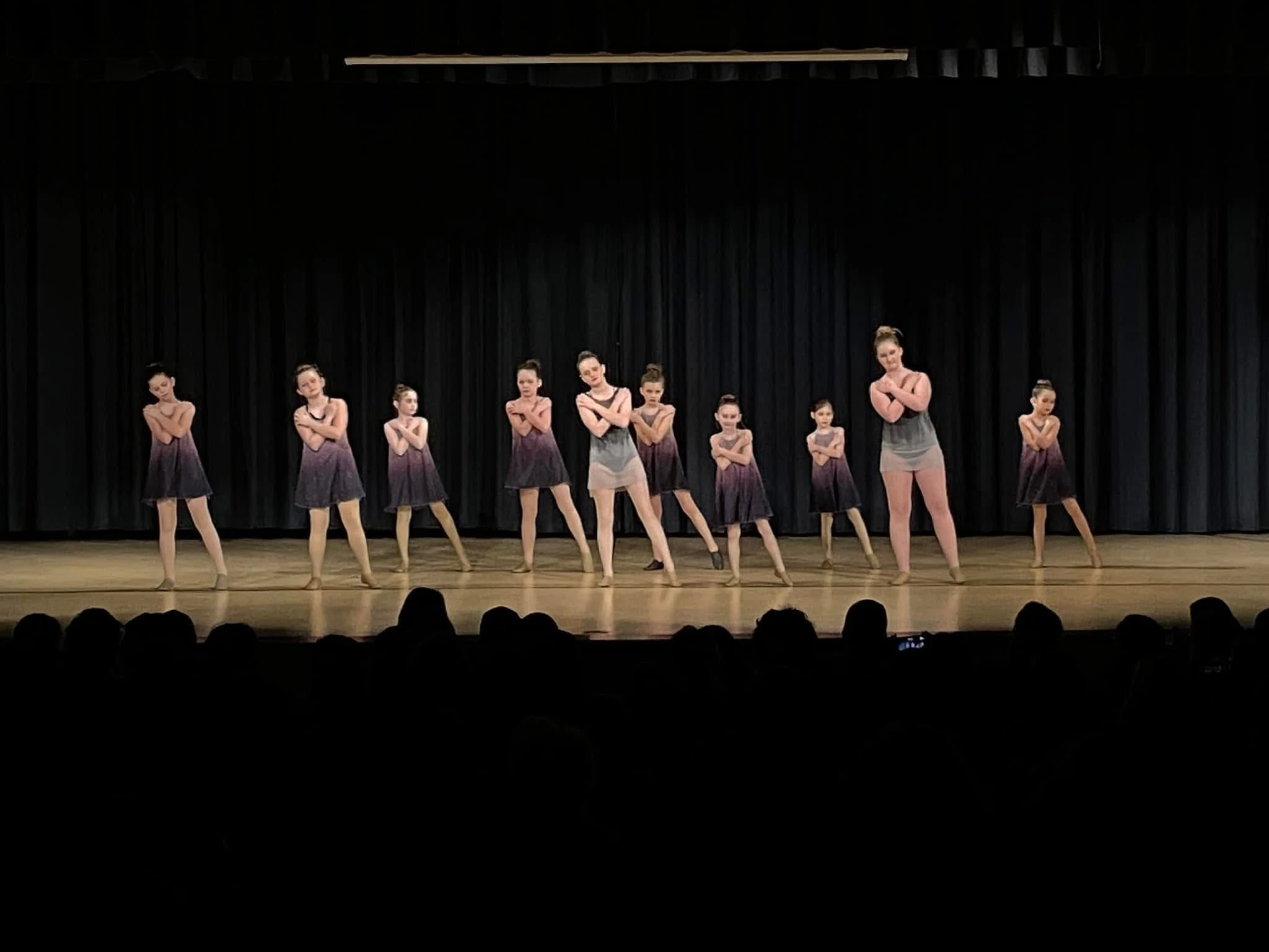 A group of dancers performing synchronized choreography on a recital stage